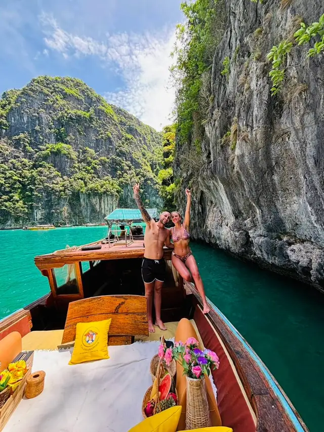 Couple on a luxury longtail in a green bay under cliffs