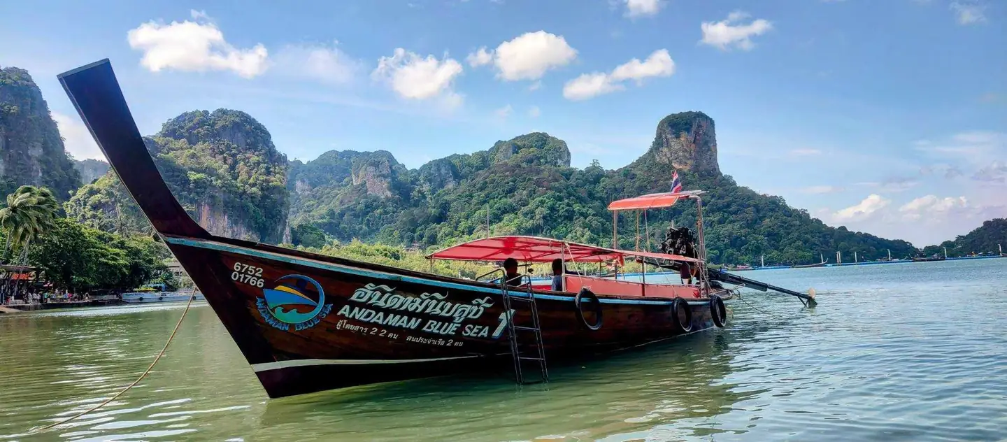 Longtail boats lined up on the beach below limestone islands