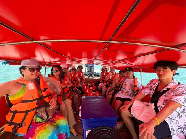 นักท่องเที่ยวใส่เสื้อชูชีพในเรือหางยาวหลังคาแดง